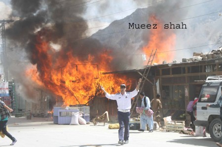 A traffic police official waves helplessly as the wooden cabins burn behind. A vendor can be seen trying to save whatever he can