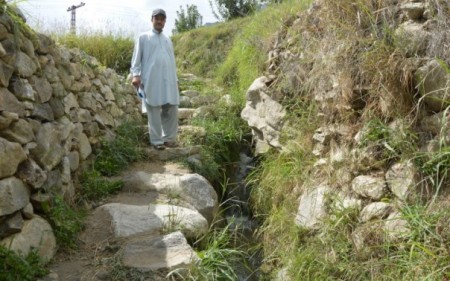 Inayat Karim, a mountain farming expert with the Baltit Rural Support Organisation, stands beside a reinforced water channel in Karimabad village, northern Pakistan. TRF/Saleem Shaikh