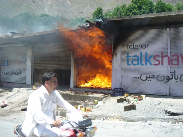 چترال، ایک شخص موٹر سائیکل پر جلتی ہوئی دکان کے سامنے سے گزر رہا ہے۔ 